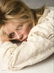 Model Marlijn Hoek resting her head, wearing an off-white embroidered lace blouse in a close-up portrait.