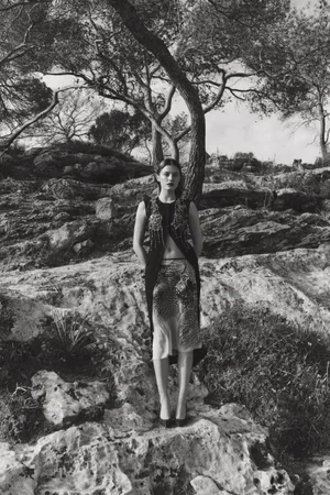 Emma Todt stands on rocky terrain in an embellished dark vest and patterned skirt under pine trees for Sèduction Magazine.
