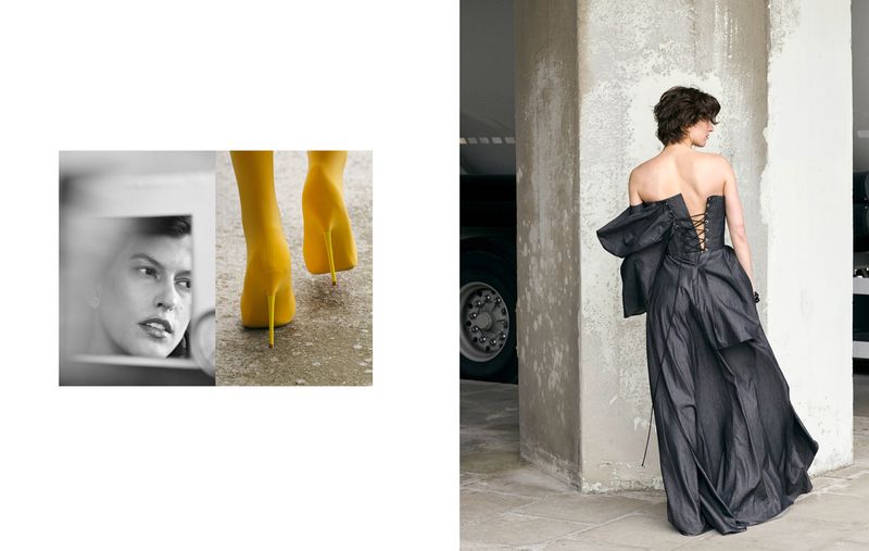 Woman in dark strapless dress with oversized bow poses in industrial setting; yellow high heels & a reflection also in the scene.