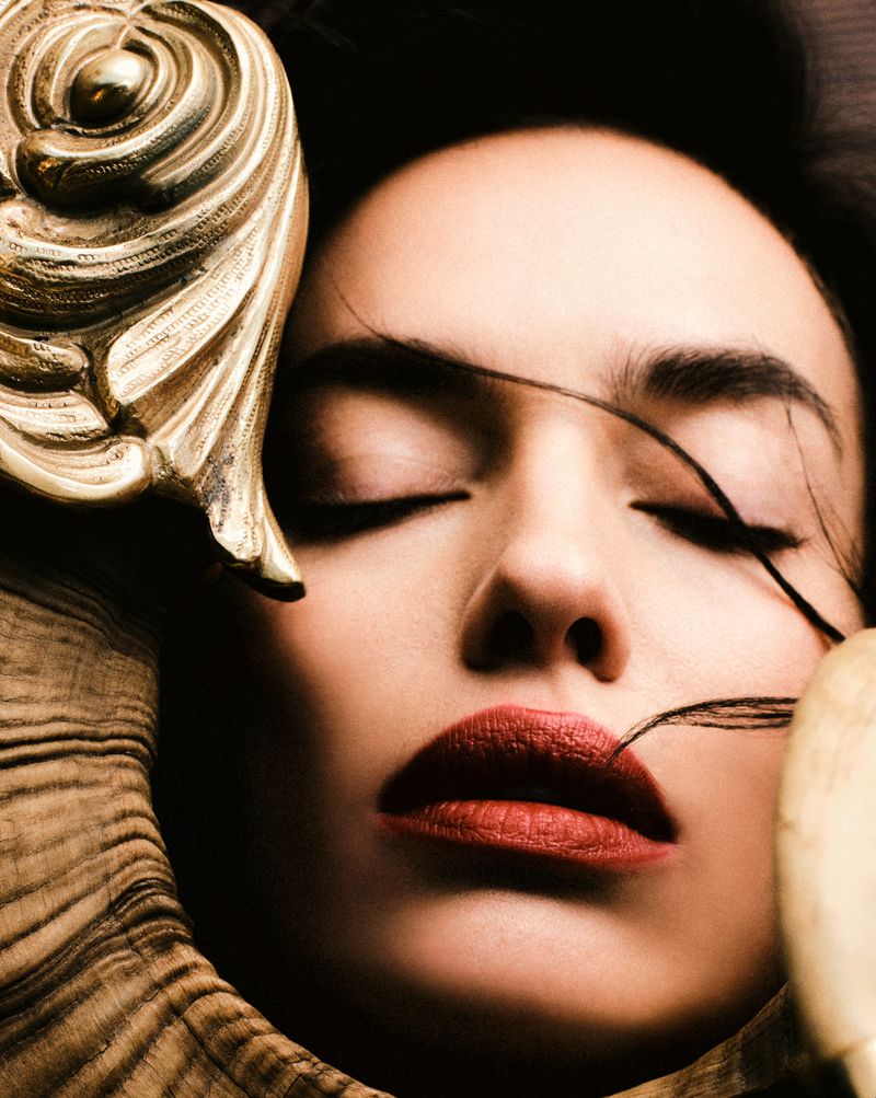 Close-up portrait of a woman with closed eyes, red lipstick, and decorative gold elements. Fashion and beauty photography.