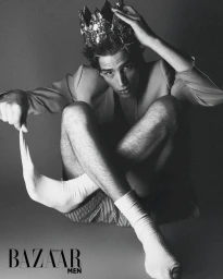 Model wearing a jeweled crown and white socks holding a sock hem against a grey studio backdrop.