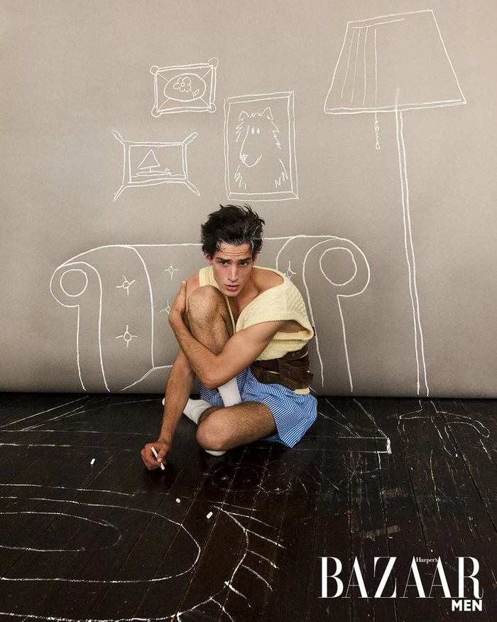 Model sitting on dark wood floor drawing with chalk against a grey backdrop with chalk sketches of furniture