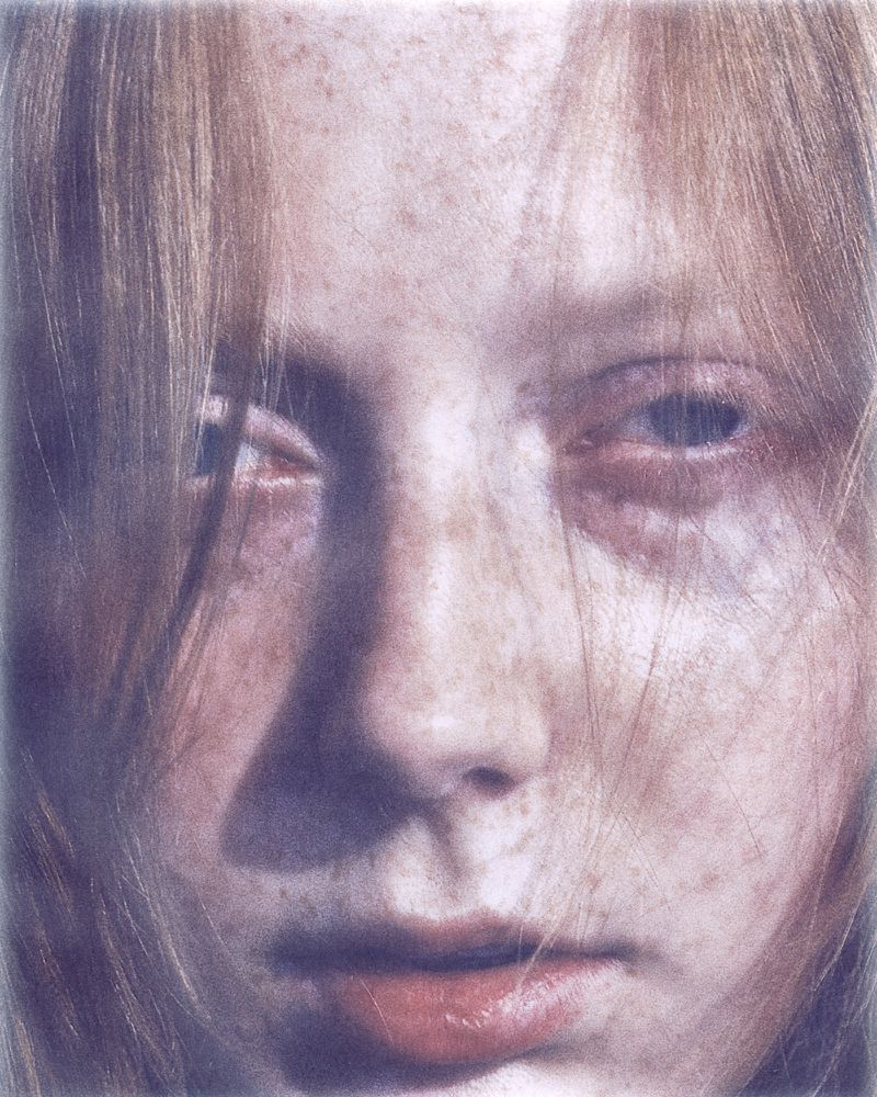 Close-up portrait of a fair-skinned, freckled woman with light hair looking directly at the camera in a hazy, dreamlike composition.