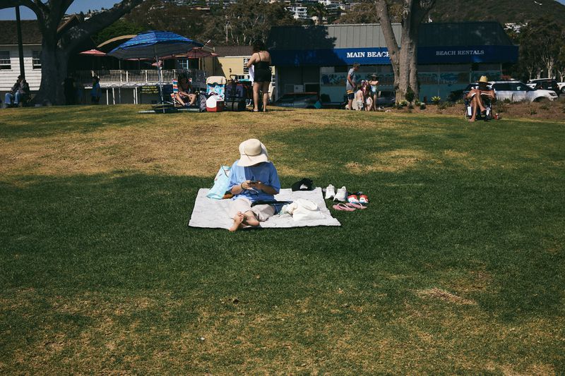 Woman relaxing on blanket in park on sunny day near beach. People enjoying outdoor recreation.