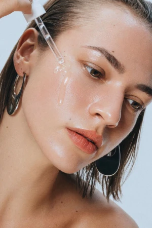 Close-up shot of a young adult female applying face serum with a dropper, showcasing beauty and skincare in a studio setting.