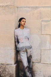 Model leaning against a weathered stone wall wearing an embellished patterned jacket and matching printed trousers