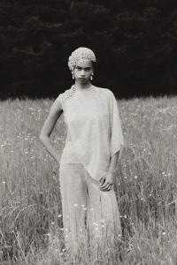 A model wearing beaded haute couture clothing and a matching headpiece standing in a grassy meadow.