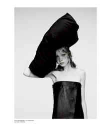 Model wearing a black strapless dress and a large black hat with a dotted veil against a seamless white studio background