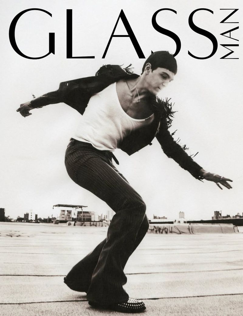 Magazine cover featuring a person in motion wearing a jacket, tank top, and trousers, set against a neutral sky and distant cityscape.
