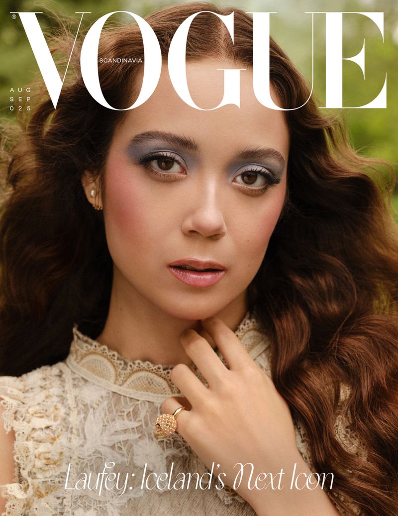 Magazine cover featuring a young woman with long brown hair and grey eyeshadow, wearing a white lace dress against a blurred green background.
