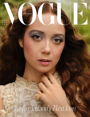 Magazine cover featuring a young woman with long brown hair and grey eyeshadow, wearing a white lace dress against a blurred green background.