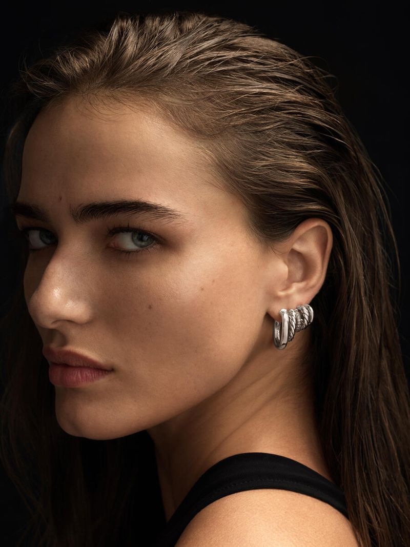 Close-up studio portrait of a young woman with brown hair and silver earrings against a dark backdrop, fashion and beauty.