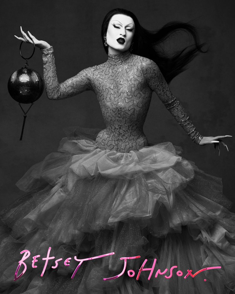 Black and white portrait of a person in a high-necked, long-sleeved dress with a full skirt, holding a disco ball.