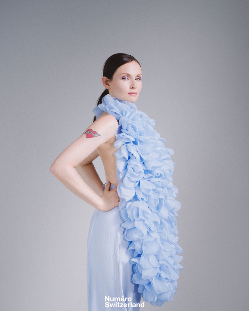 Elegant woman in a light blue dress with a floral ruffle posing in a studio, fashion editorial shot.