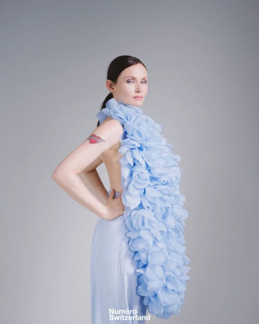Elegant woman in a light blue dress with a floral ruffle posing in a studio, fashion editorial shot.