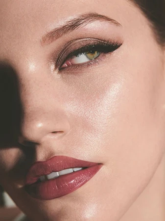 Close-up portrait of a woman's face, showcasing glossy red lips, defined eyeliner, and soft, natural makeup. Professional beauty shot.