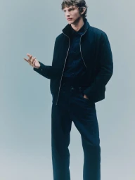 Male model wearing a dark navy zip jacket and matching trousers against a pale grey seamless studio backdrop.