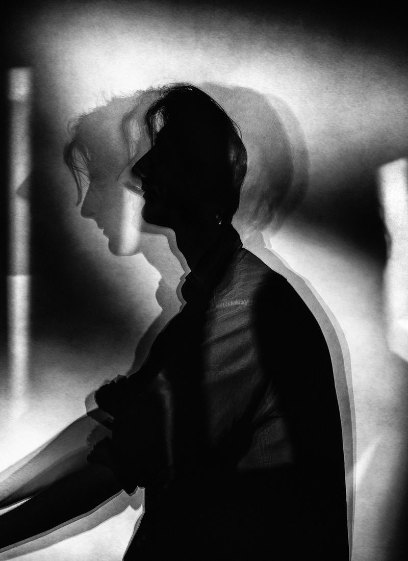 Monochrome portrait of an adult with long hair, captured in a photo studio using multiple exposure and silhouette techniques.