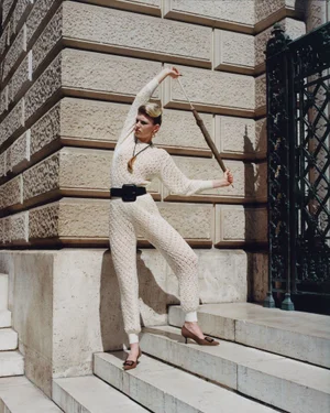 Model in cream knit jumpsuit with a thick black belt holding an umbrella on stone steps
