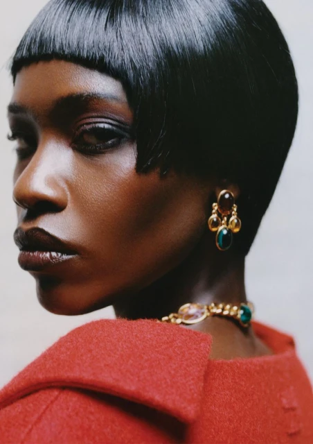 Close-up studio shot of a woman with short black hair wearing a red jacket, gold necklace and earrings. Fashion Beauty shot.