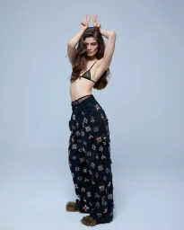 Model Merlijne Schorren posing in an embellished black pant and lace bralette against a seamless grey backdrop for Elle U.S. It Girl
