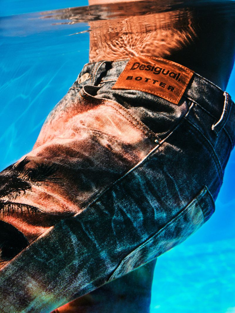 Person wearing jeans underwater in a pool with light reflecting on the surface, showing water movement and clothing details.