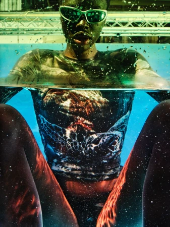 A model submerged in a water tank wearing green sports sunglasses and an aquatic print shirt.