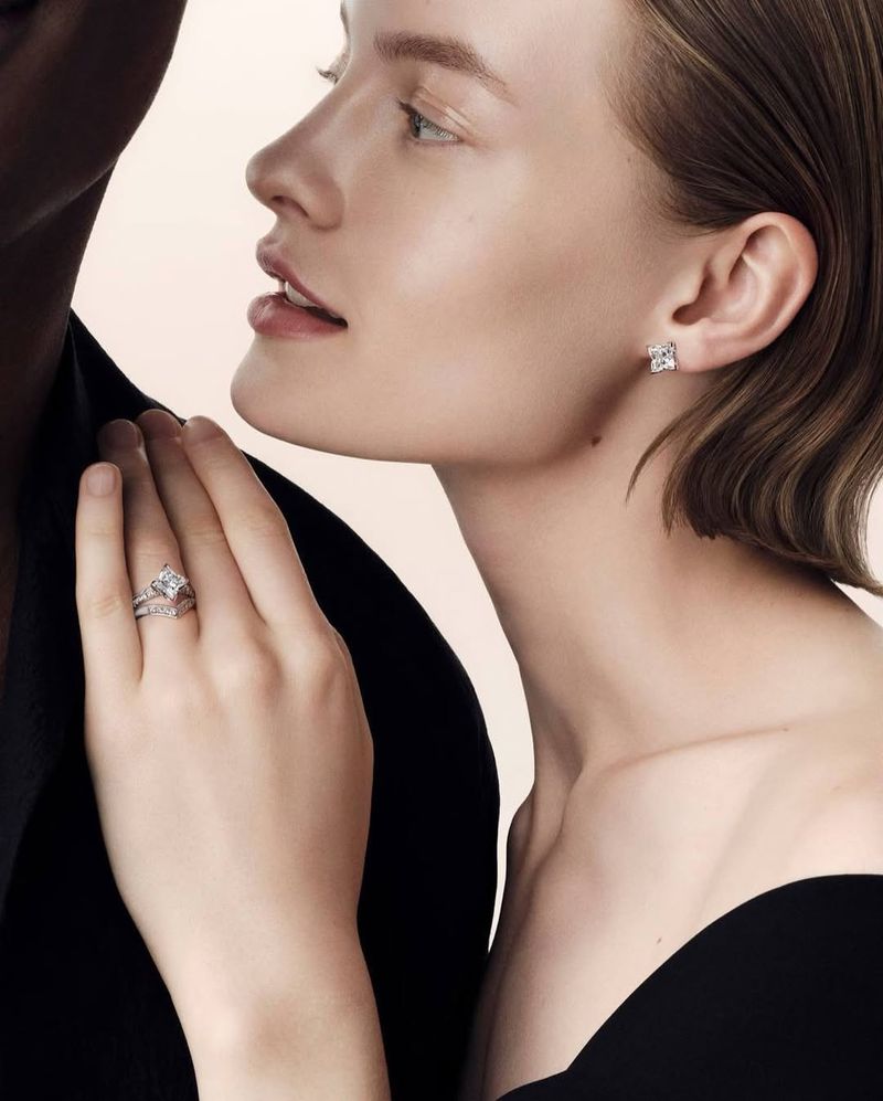 Jewellery advertisement featuring a fair-skinned adult woman wearing square diamond earrings and a ring alongside a dark-skinned person.