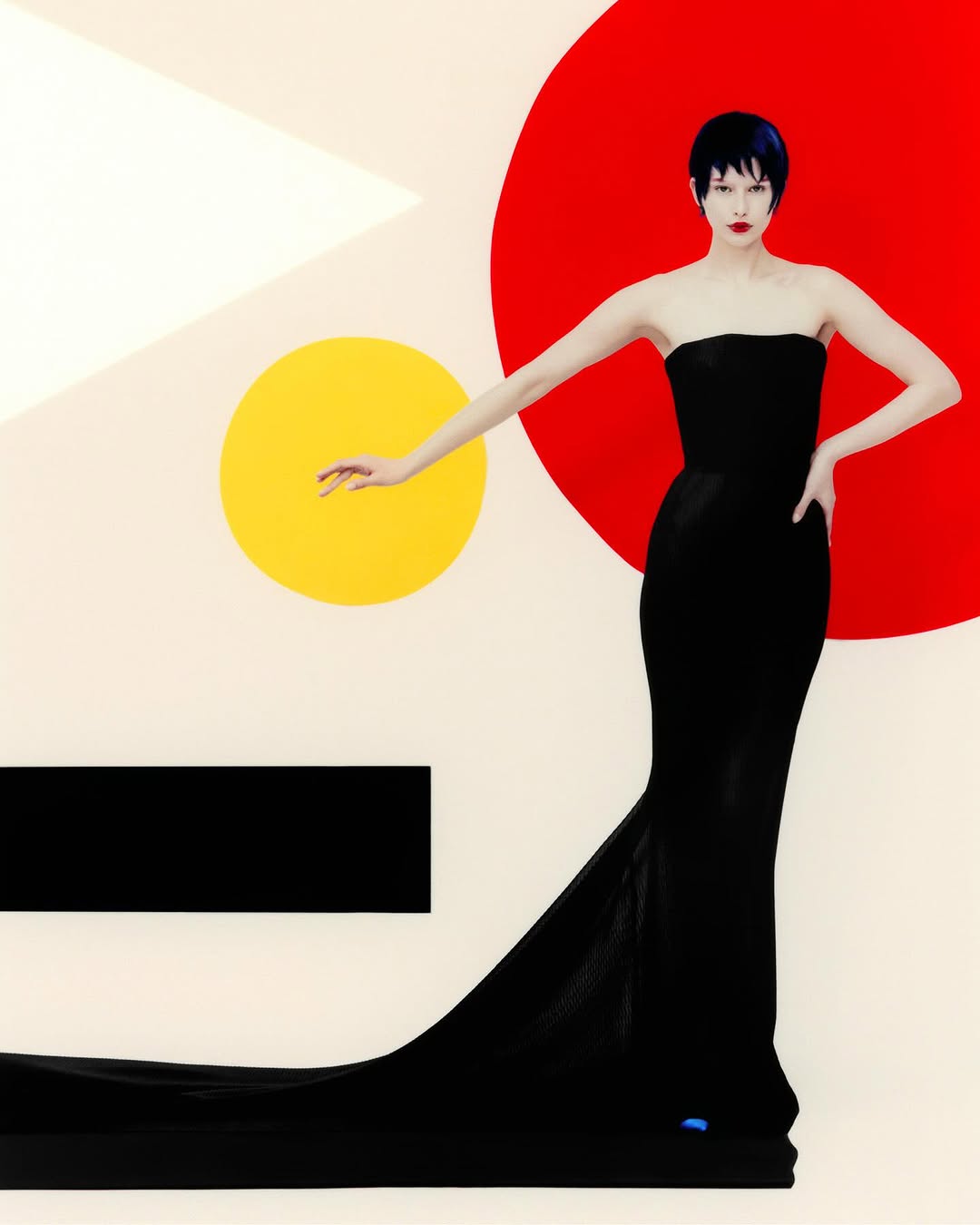 Elegant adult female with short dark hair in a strapless black gown posing against a modern graphic backdrop of shapes and vibrant colors.