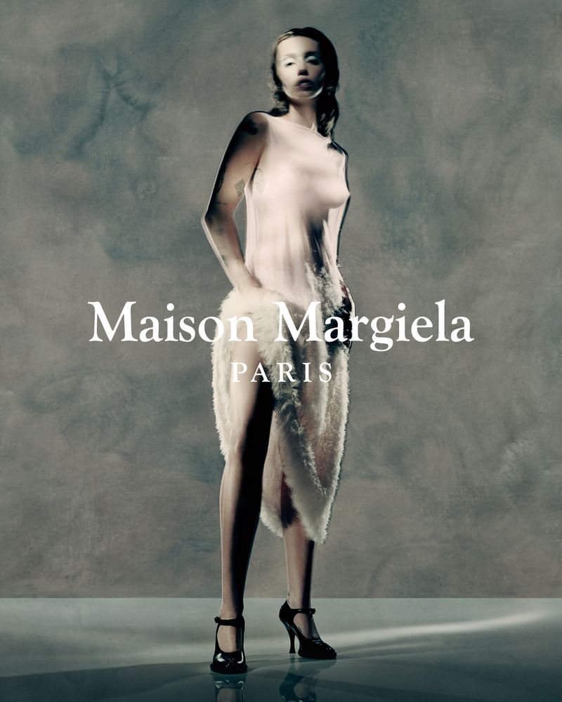 Fashion shot of a woman wearing heeled shoes and a light-colored, furry garment, posing in front of a textured grey background.