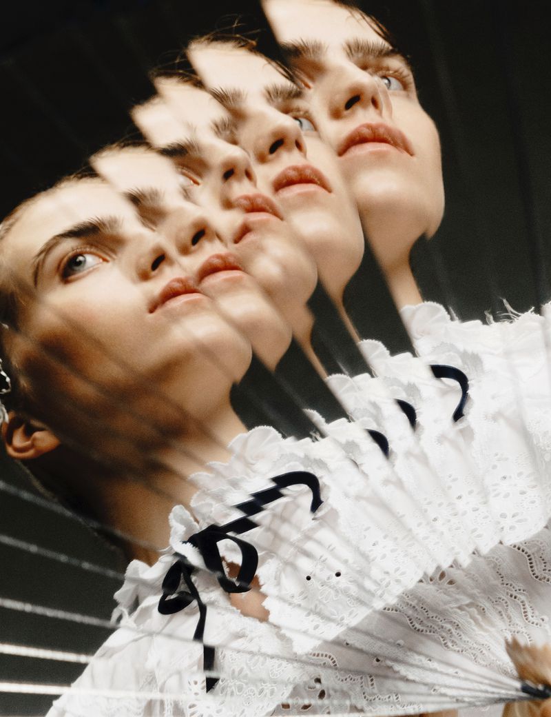 Multiple exposures of a young woman with fair skin in a white lace top, looking up, holding a white lace fan against a dark background.