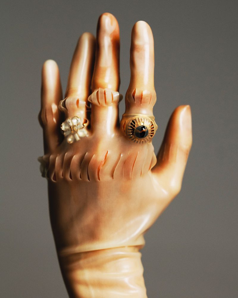 Antique ivory hand sculpture adorned with decorative rings on fingers and wrist, presented against a neutral background.