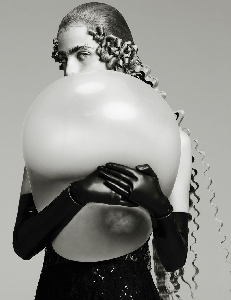 Striking black and white portrait of a woman partially hidden behind a large, round balloon, wearing long gloves and a dark dress.
