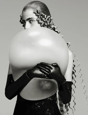 Striking black and white portrait of a woman partially hidden behind a large, round balloon, wearing long gloves and a dark dress.