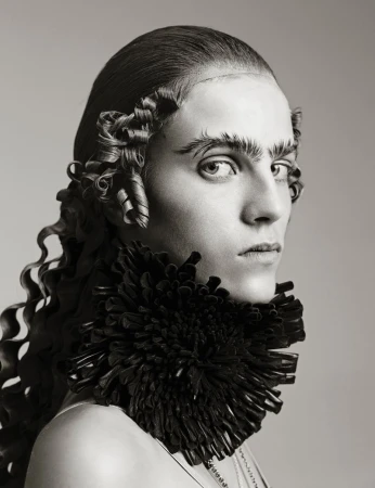 Close-up portrait of a person with an elaborate hairstyle, dark ruffled collar, and serious expression in a studio environment.