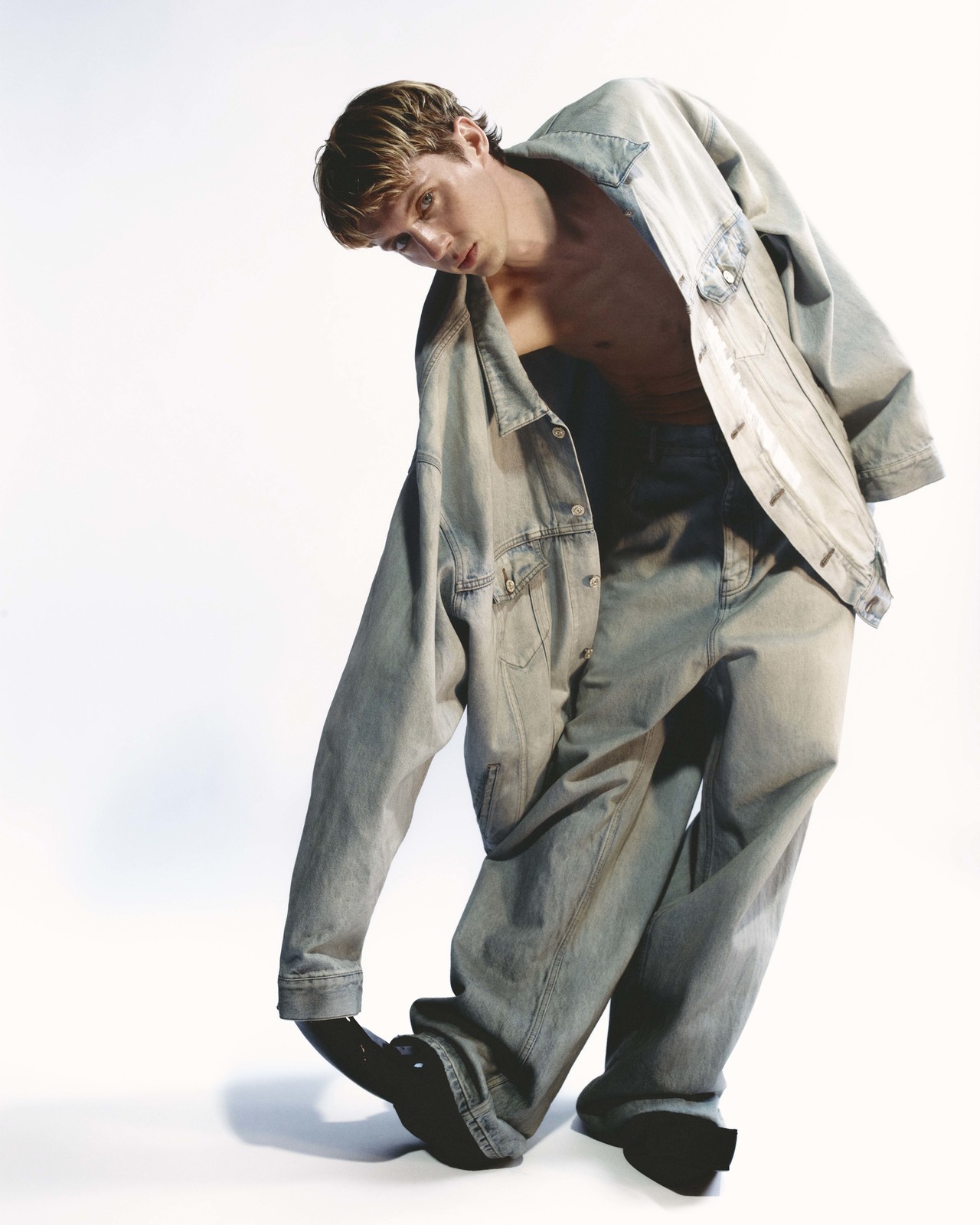 Young man wearing an oversized denim jacket and jeans posing against a plain white background