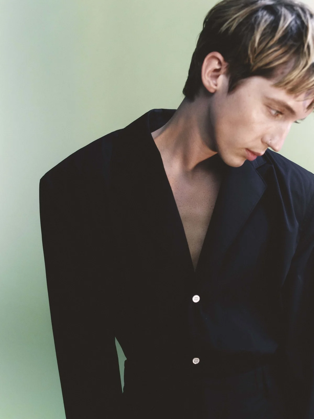 Portrait of singer Troye Sivan wearing a black tailored jacket against a pale green background