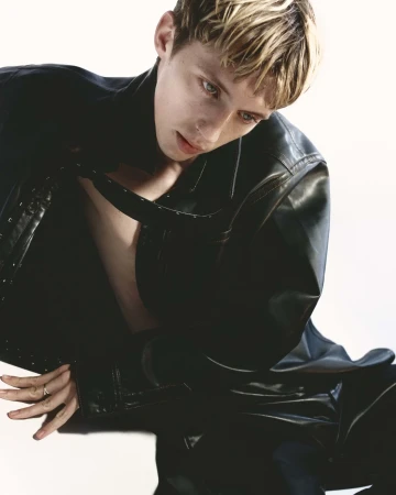 Troye Sivan wearing a black leather jacket against a bright white background
