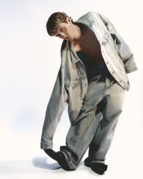Young man wearing an oversized denim jacket and jeans posing against a plain white background