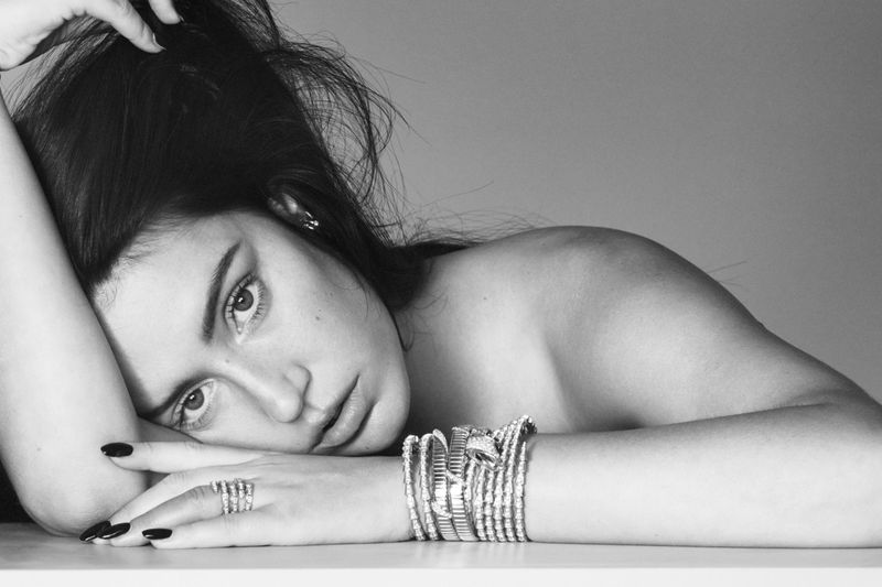 Monochrome portrait of a young adult woman lying down, adorned with multiple silver bracelets and rings. Focus on facial expression.