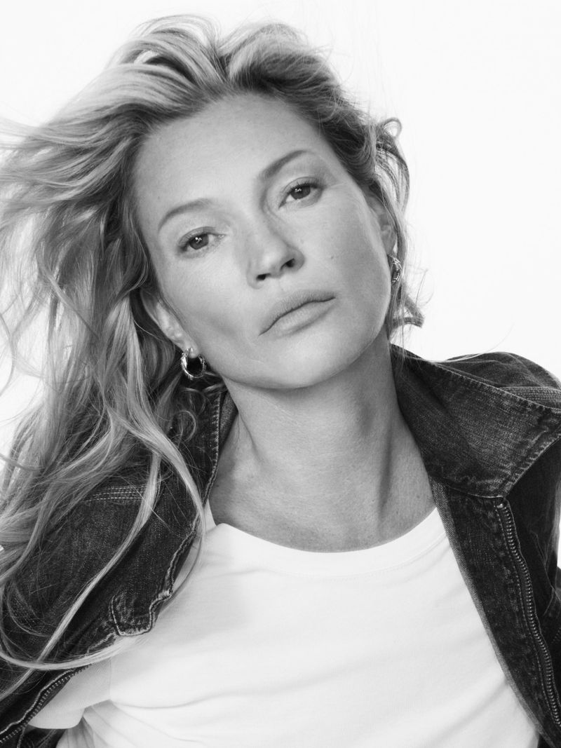 Black and white portrait of a woman with wavy blonde hair wearing a denim jacket and white shirt against a white backdrop.