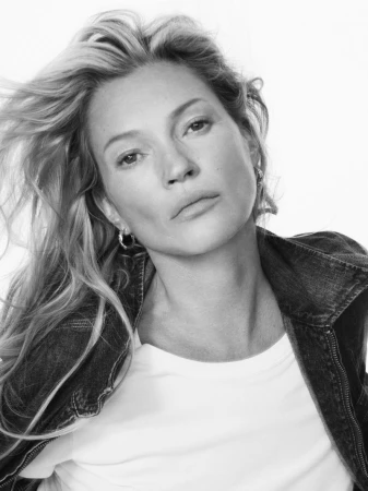 Black and white portrait of a woman with wavy blonde hair wearing a denim jacket and white shirt against a white backdrop.