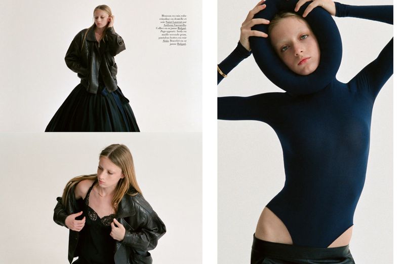 Editorial fashion shot of a young woman in a dark blue leotard, black leather jacket and skirt, against a neutral backdrop.