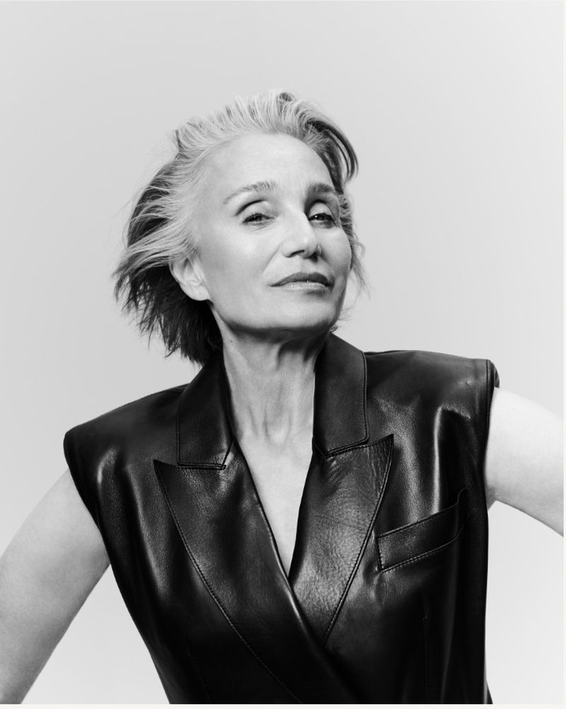 Actor Kristin Scott Thomas wearing a black sleeveless leather vest against a light grey studio background.