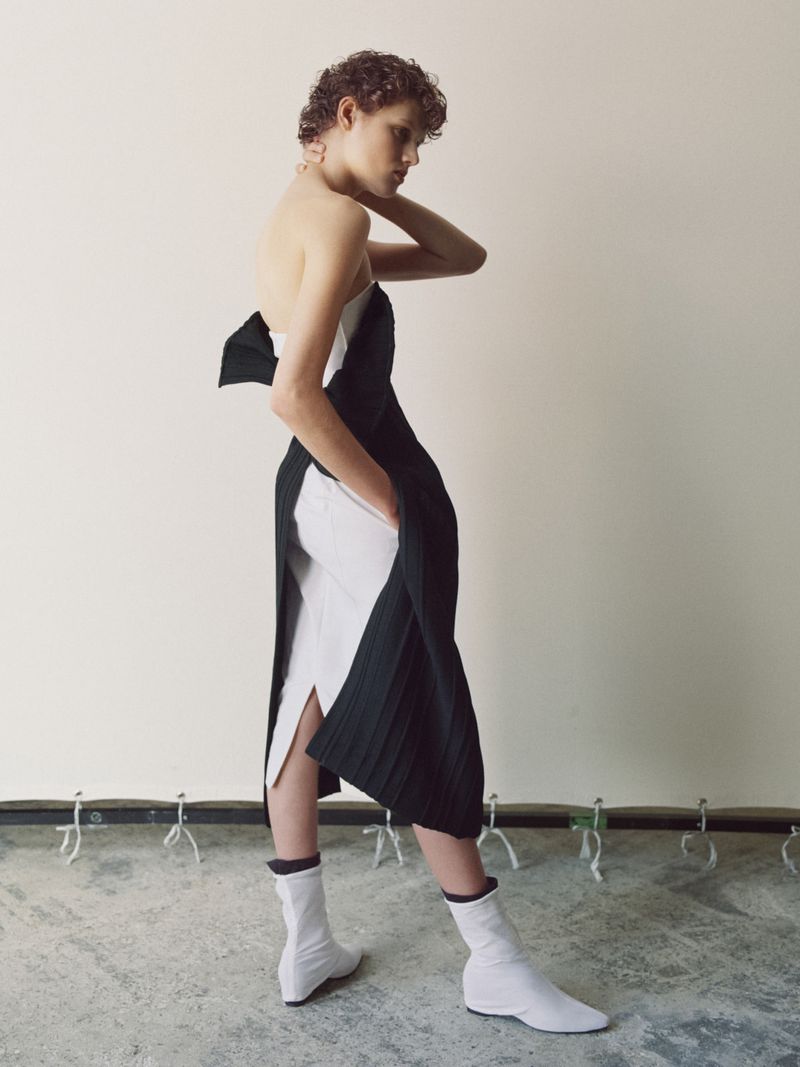 Elegant woman in a black and white strapless dress with white ankle boots posing in a studio. Fashion shot with a minimalist backdrop.