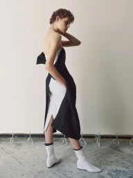 Model in a black structured dress over a white outfit wearing white boots standing against a neutral backdrop