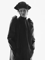 Model wearing a structured dark coat and hat against a bright white background for Harper's Bazaar U.S.