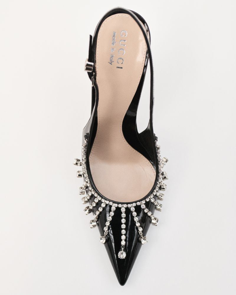 Elevated view of a glossy black slingback high heel pump from Gucci, featuring an elegant jeweled fringe on a white backdrop.