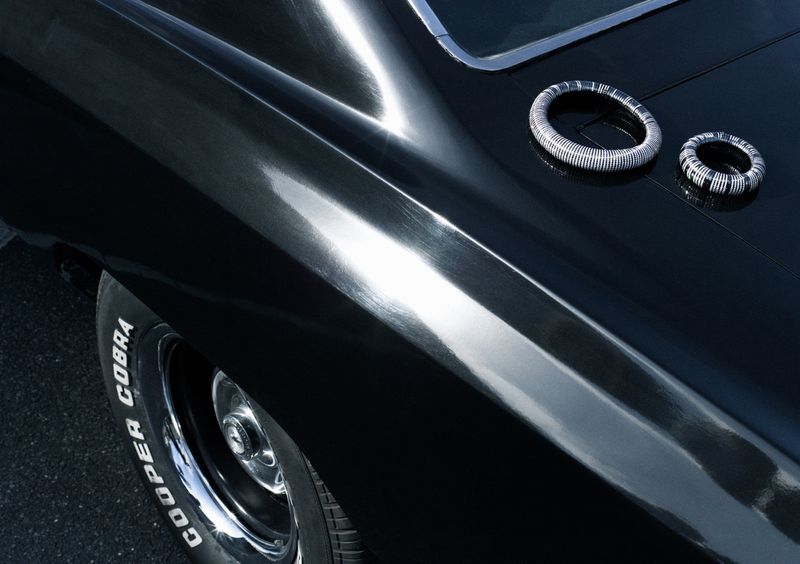Close-up of a sleek, black classic car showcasing its glossy finish, tire with white lettering, and chrome accents.
