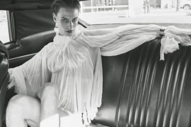 Model Veronika Kunz in a pleated white blouse seated inside a car for Vogue Ukraine Vertigo project